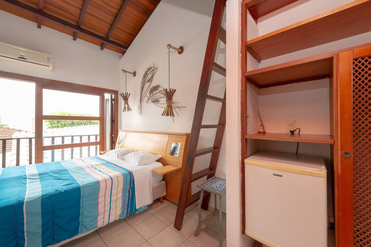Ein Schlafzimmer mit einem Bett, einer Holzleiter, einem kleinen Tisch und einem Minikühlschrank.