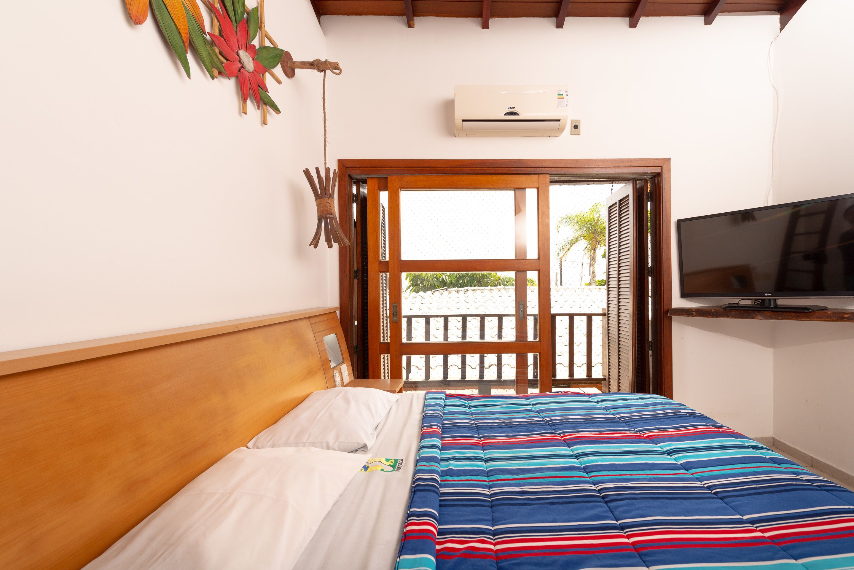 Quarto com cama, televisão e janela com vista para palmeiras.