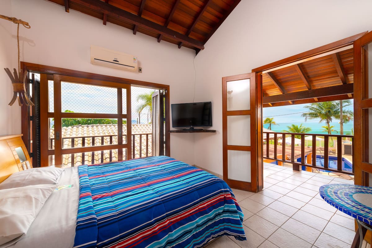 Ein Schlafzimmer mit Bett, Fernseher und einem Balkon mit Meerblick.