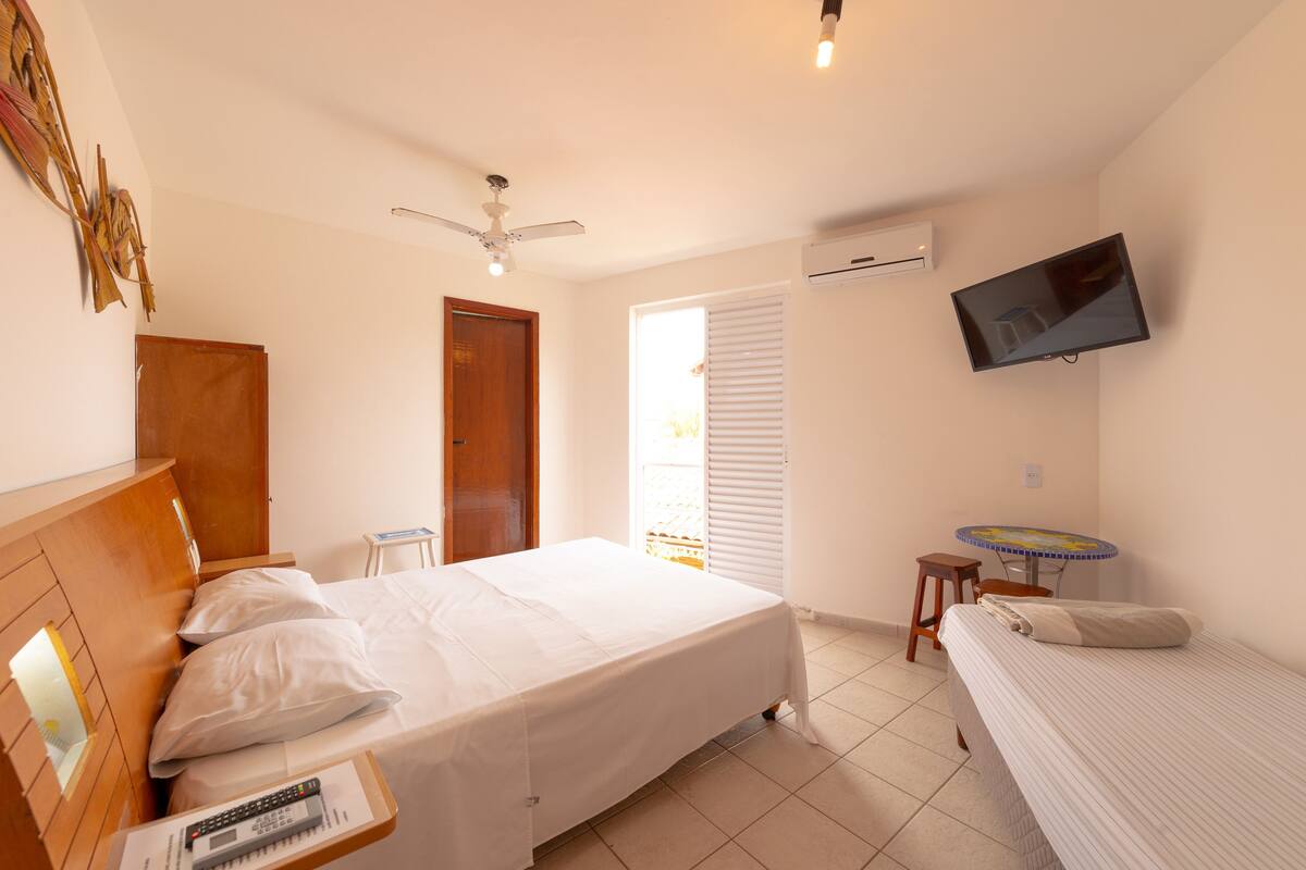 Ein Schlafzimmer mit Bett, Deckenventilator, Fernseher, kleinem Tisch und Fenster mit Jalousien.
