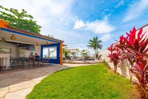 Un patio al aire libre con suelo de piedra, césped y una zona de piscina con sillones de descanso y sombrillas.