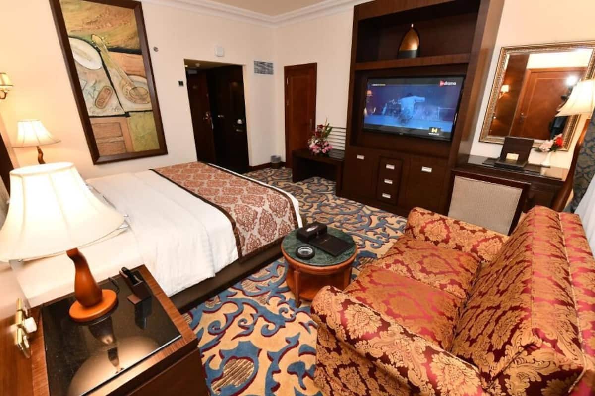 Een hotelkamer met een bed, een slaapbank, een televisie, een lamp en een schilderij aan de muur.