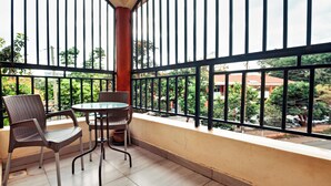 Een balkon met een tafel en twee stoelen, een uitzicht op de stad door een metalen hekwerk, en een betegelde vloer.