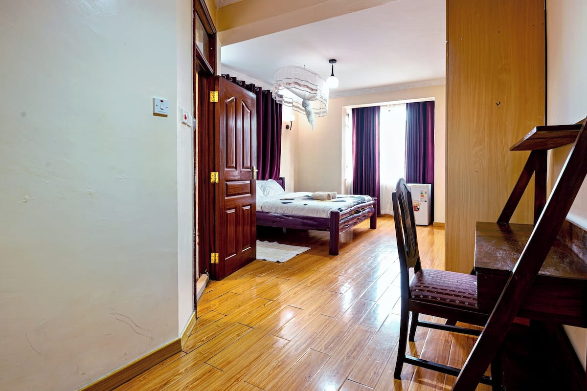 A bedroom with a wooden floor, a bed with a white comforter, a chair, and a wooden wardrobe.