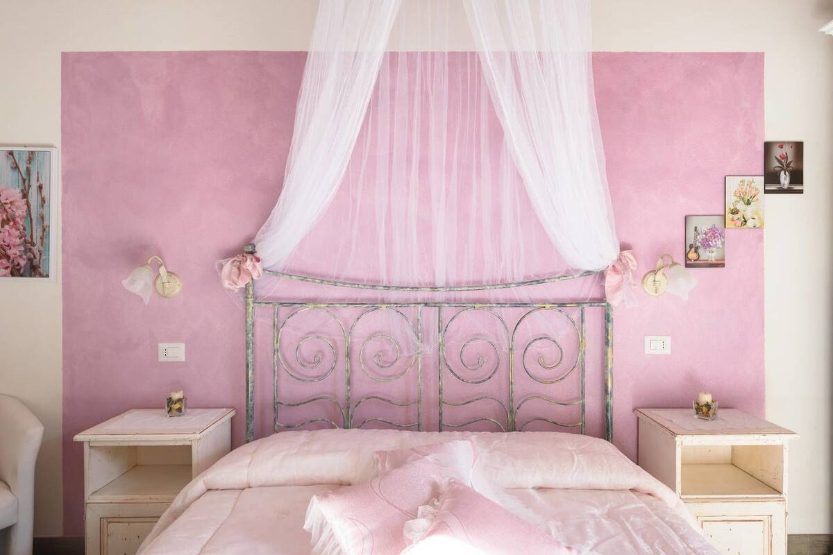 A bedroom with a pink wall, a canopy bed, bedside tables, and wall-mounted lamps.