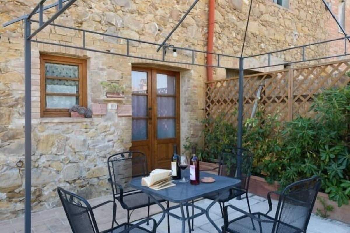 A stone building with a wooden door and windows, a table with chairs, and a lattice fence.