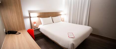 A hotel room with a bed, bedside table, chair, and a desk with a phone.