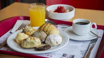 Bandeja de desayuno con bollos, un vaso de jugo de naranja, un tazón de fresas y una taza de café.