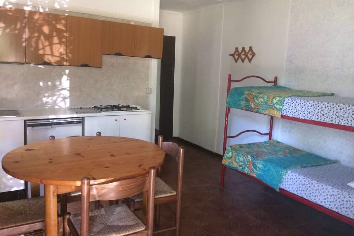A compact room with a wooden dining table, bunk beds, a kitchenette, and a patterned wall.