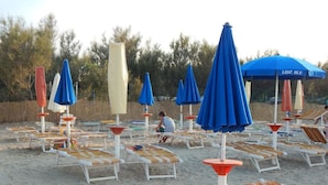 A beach with rows of sun loungers and umbrellas, some with people sitting.