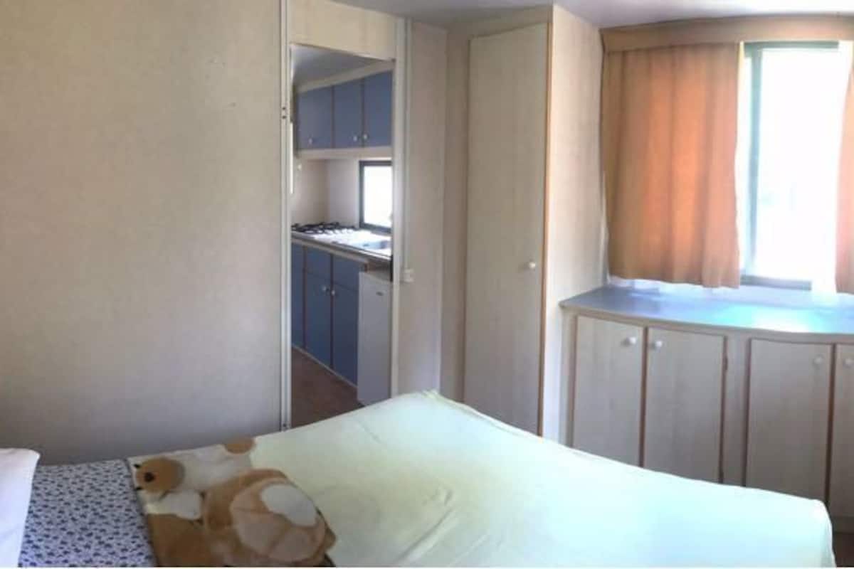 A bedroom with a bed, a window with curtains, a wardrobe, and a desk with a chair.