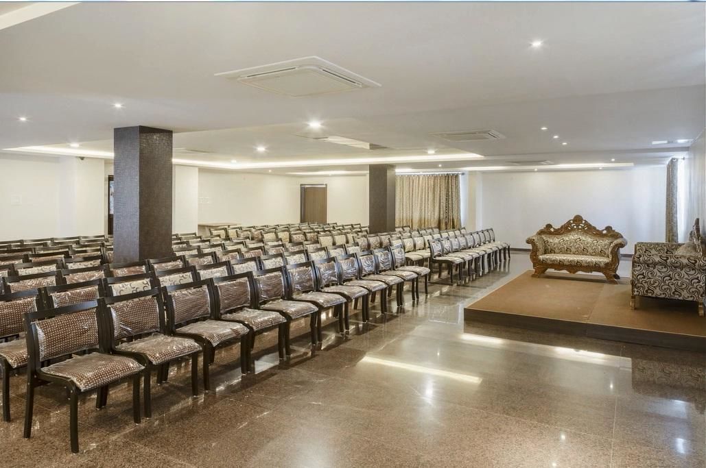 Un salón de conferencias con filas de sillas, un escenario y un pilar grande.