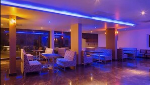 A modern lounge area with patterned sofas and tables, ambient lighting, and a polished floor. - R G Hotels and Resort (Malur)