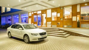 A white sedan parked in front of a hotel entrance with a checkered floor pattern and a modern design. - R G Hotels and Resort (Malur)
