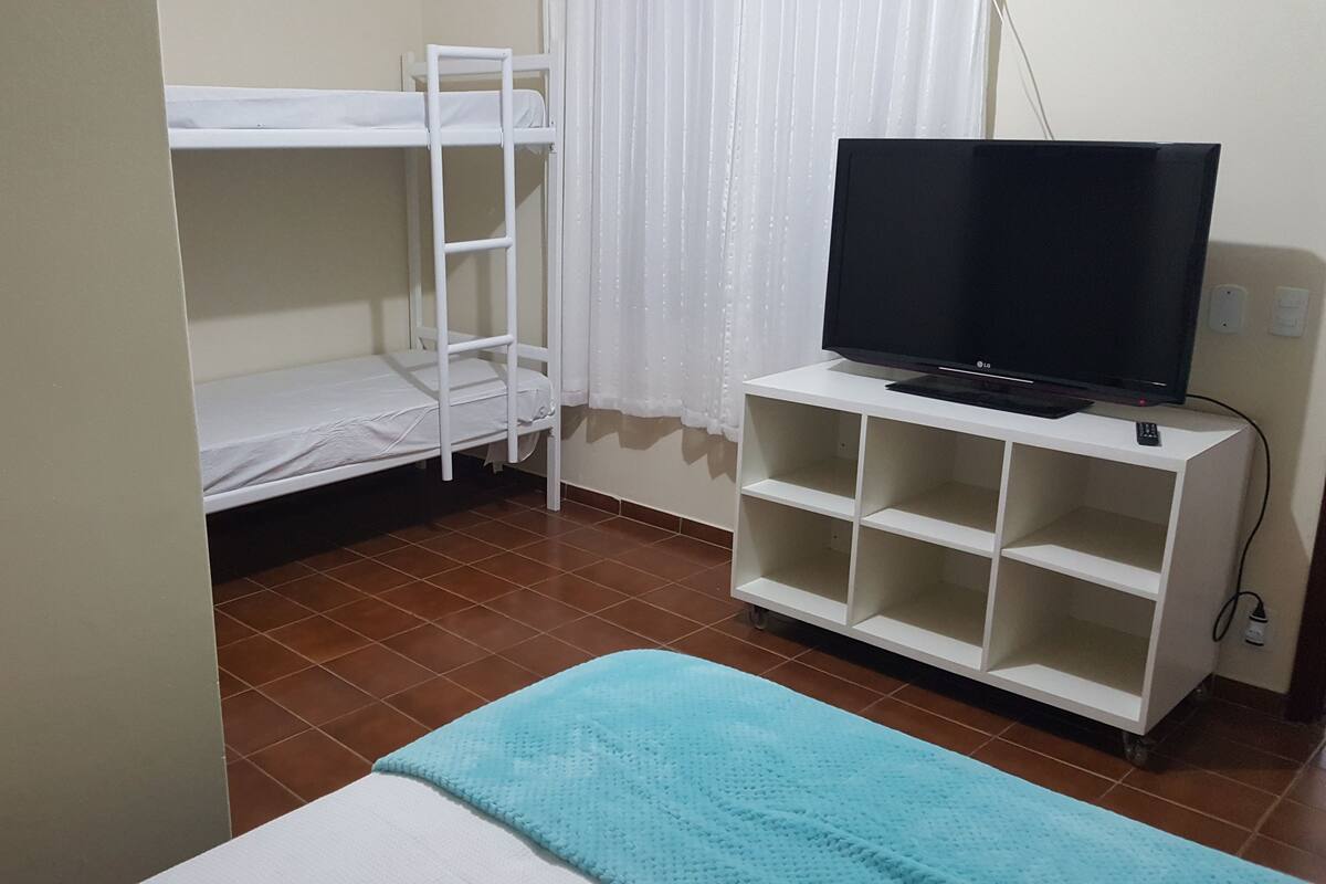 A room with a bunk bed, a television on a white stand, and a blue blanket on a bed.
