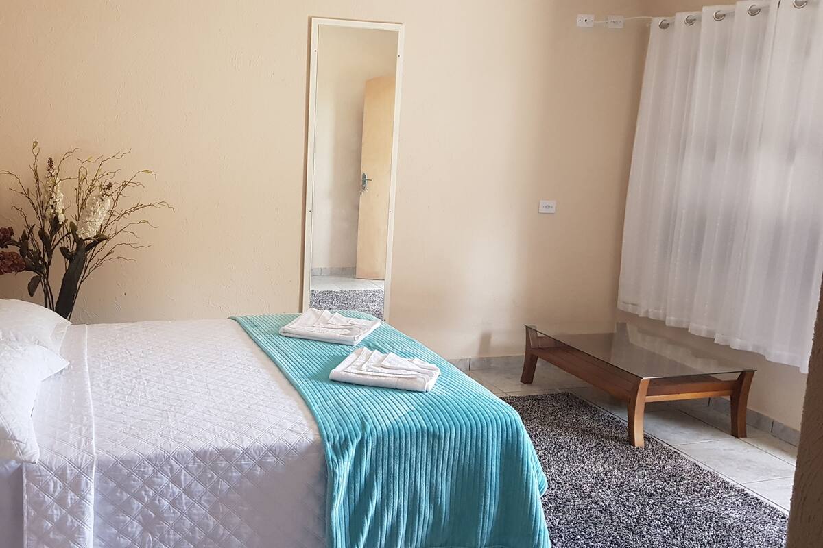 A neatly arranged bedroom with a bed, a bench, a mirror, and a vase with dried flowers.