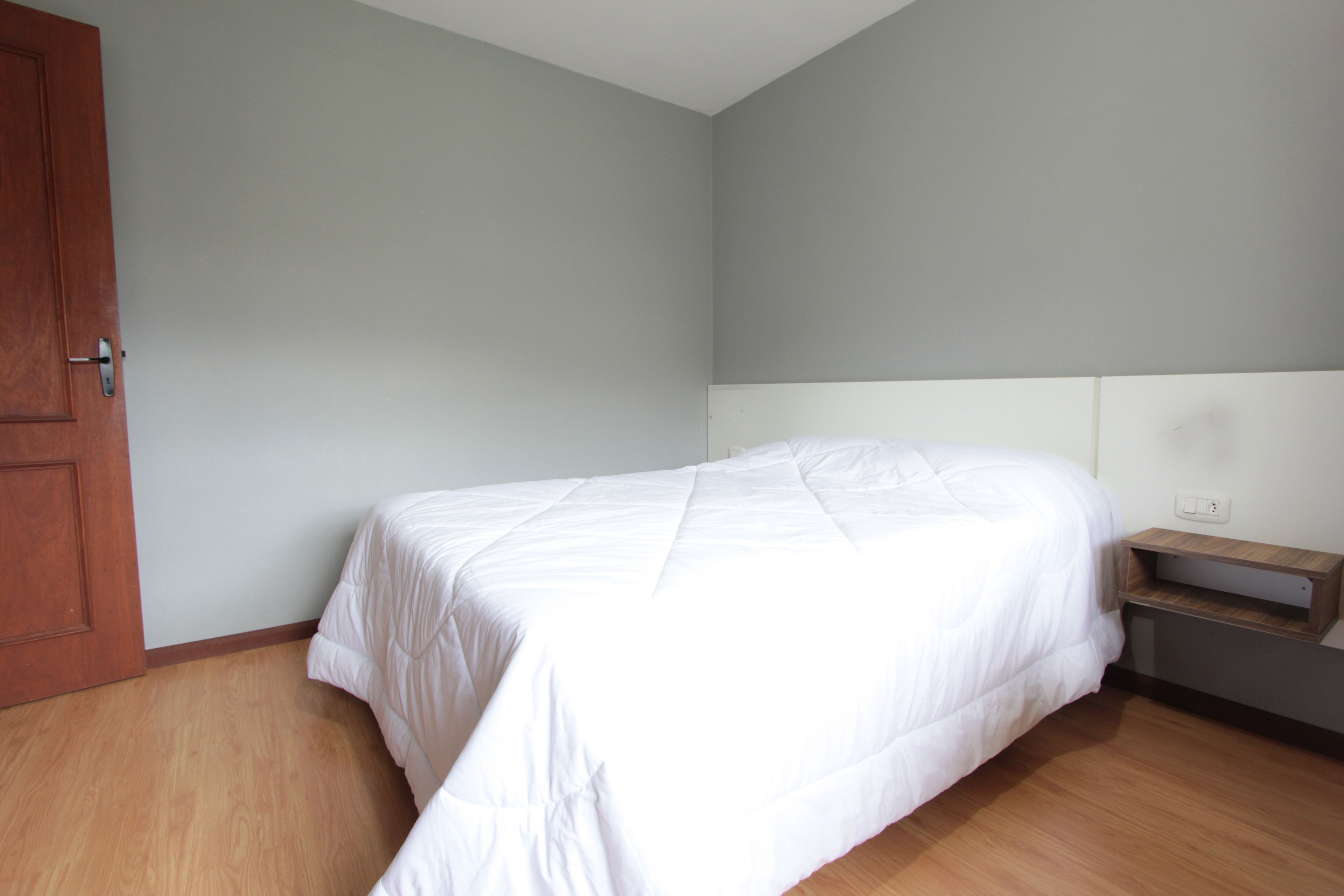 A bedroom with a bed, a wooden door, and a nightstand with a shelf.