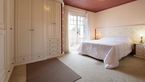 Une chambre dotée d’une grande armoire, d’un lit avec une literie blanche, d’une table de chevet et d’une fenêtre avec des rideaux.