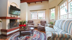 Un salon avec une cheminée, deux fauteuils, un canapé et un téléviseur fixé au mur.