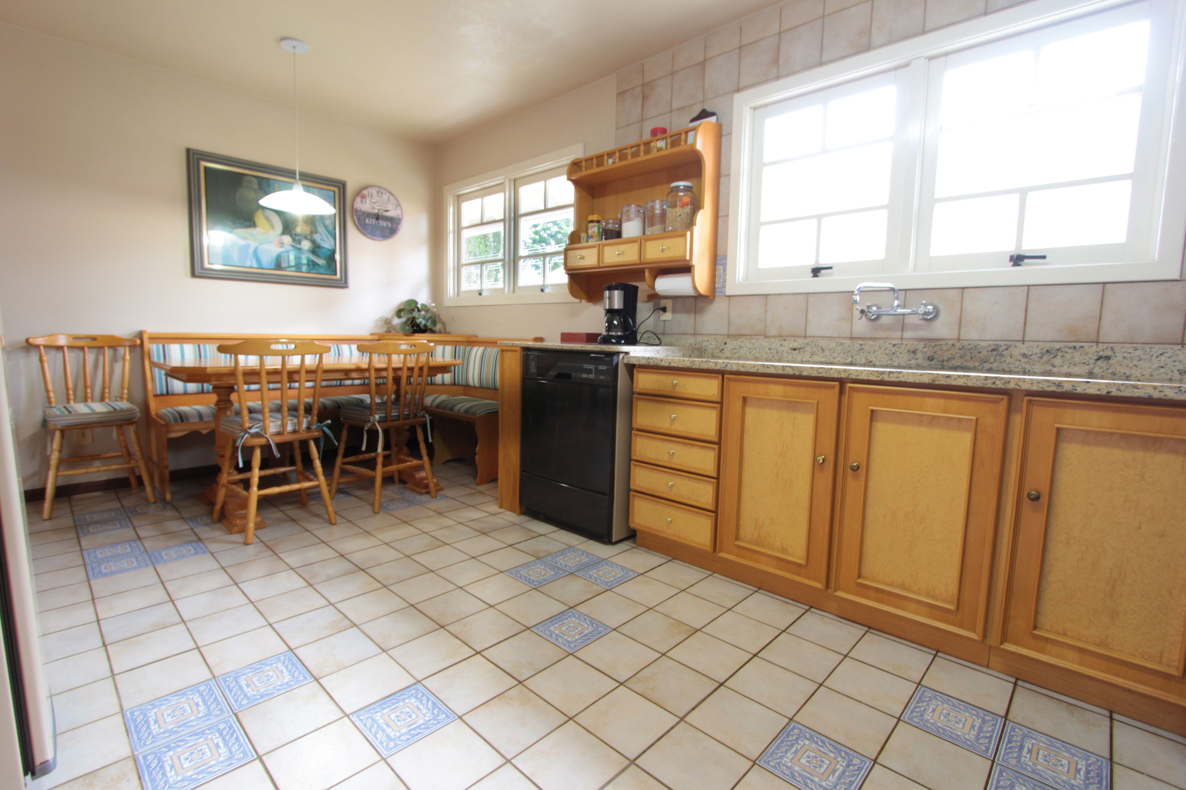 Una cocina con armarios de madera, una mesa de comedor con sillas, un refrigerador y una cafetera.