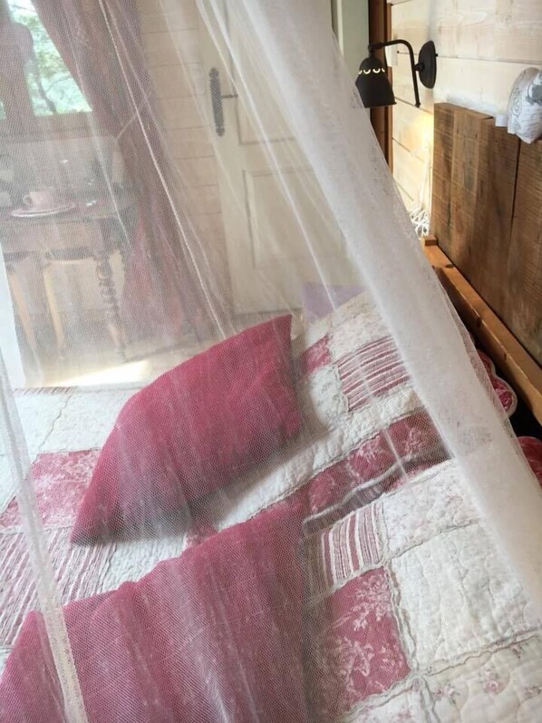 Ein Bett mit einer Bettdecke in Weiß und Rosa mit Muster, einem Holz-Kopfteil und einem weißen Baldachin.