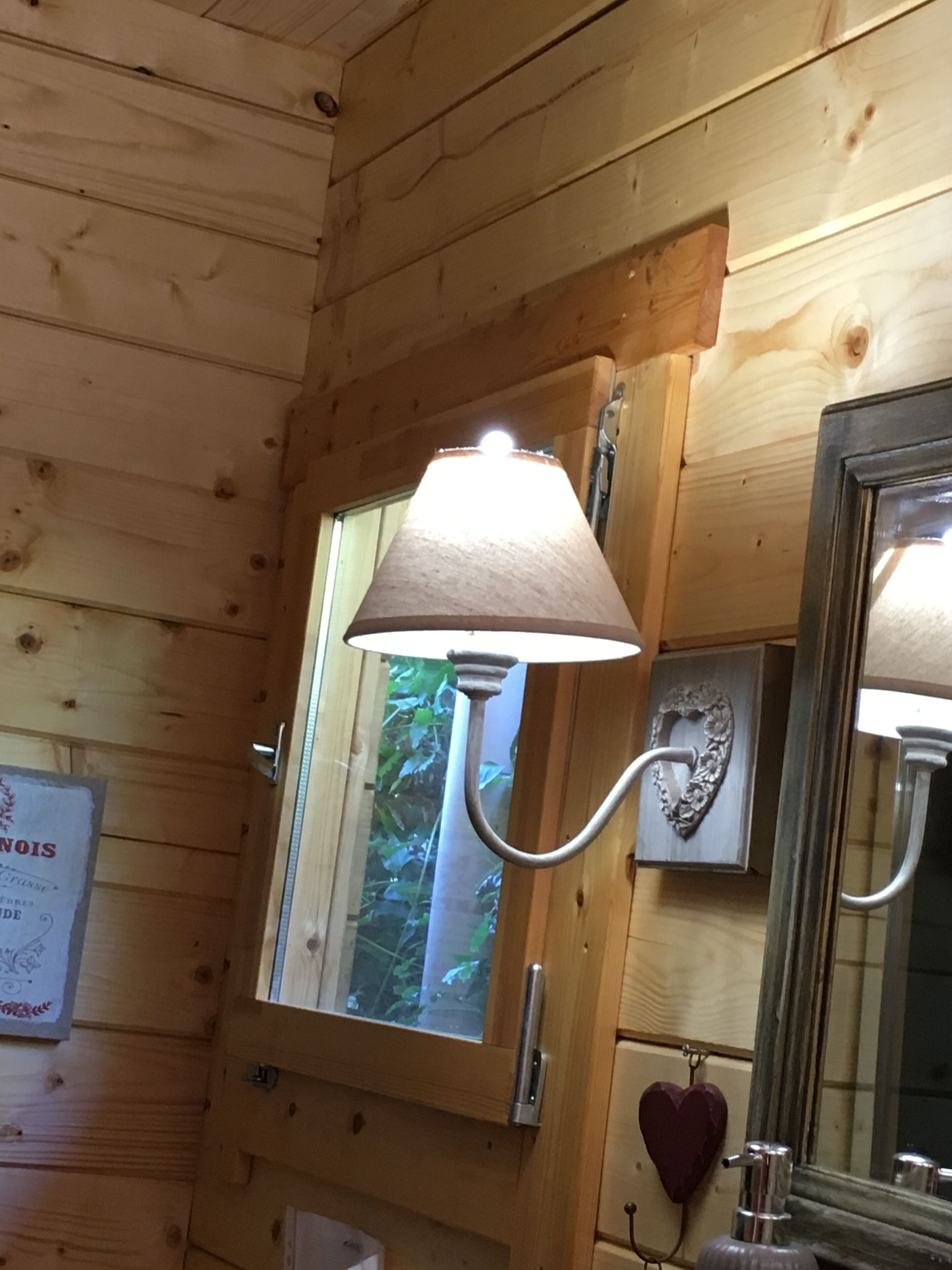 A wooden cabin interior with a window, a mirror, and a wall-mounted light fixture.