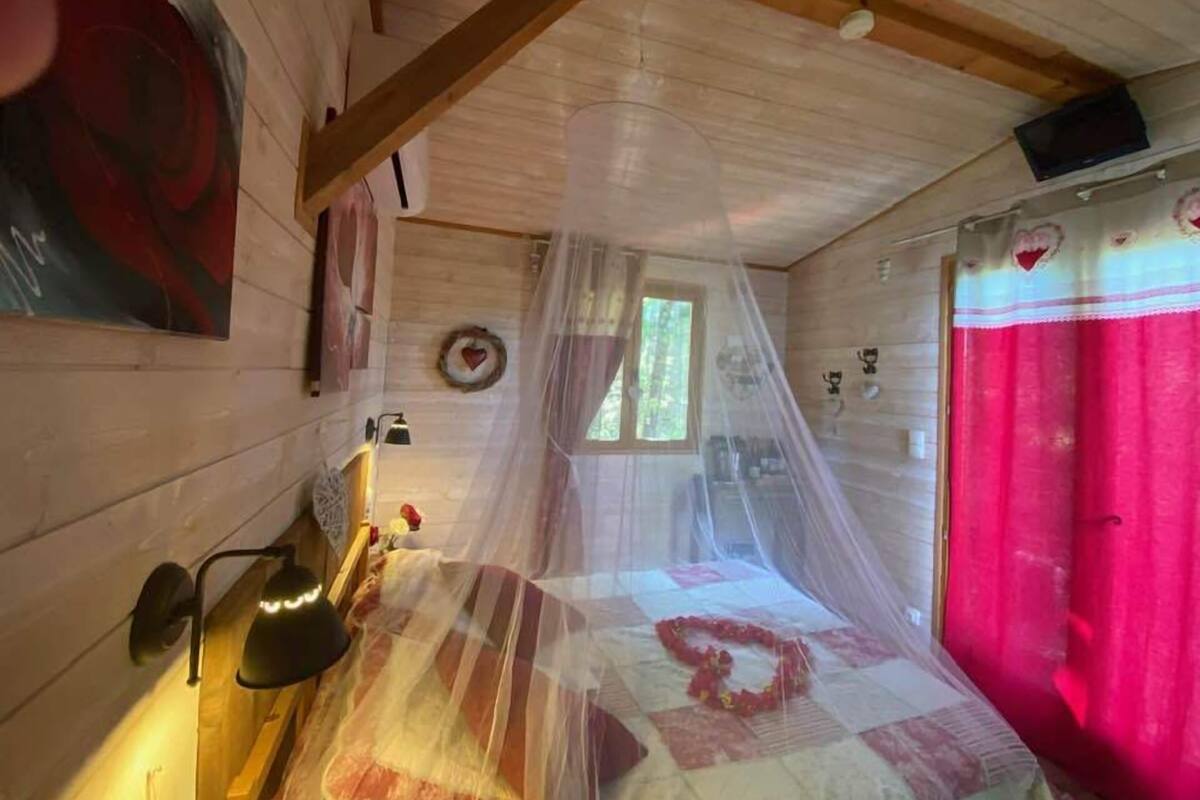 Une chambre confortable avec un lit recouvert d’une couette rouge et blanche, un plafond en bois et une fenêtre donnant sur les arbres.