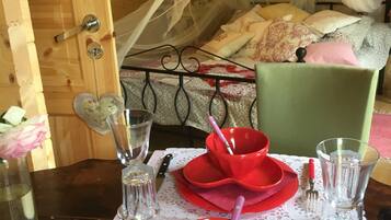 Una habitación de madera con una cama, una mesa para dos dispuesta con platos negros y rojos, vasos y cubiertos.