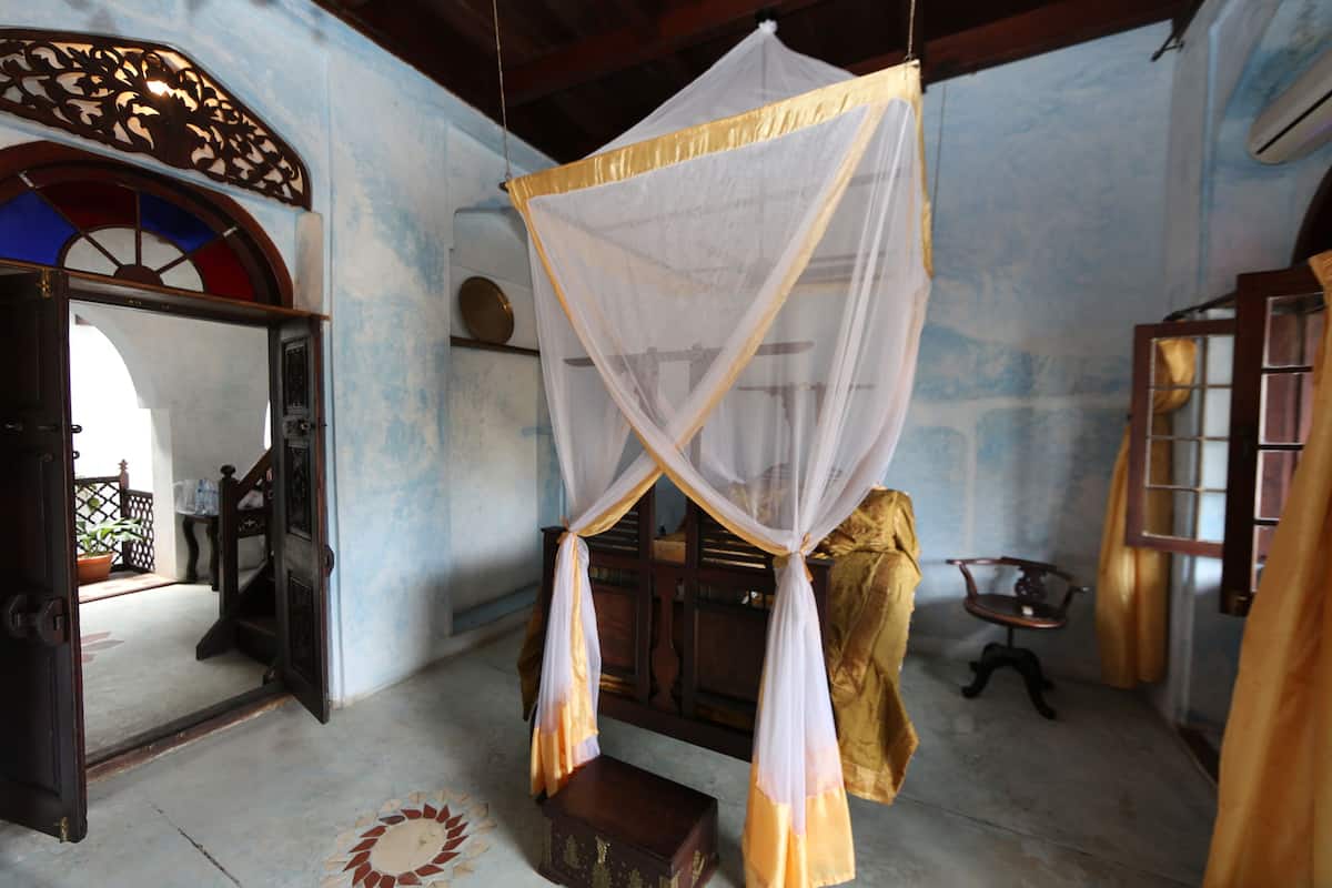 A room with a bed under a canopy, a wooden chest, a small table, and a chair.