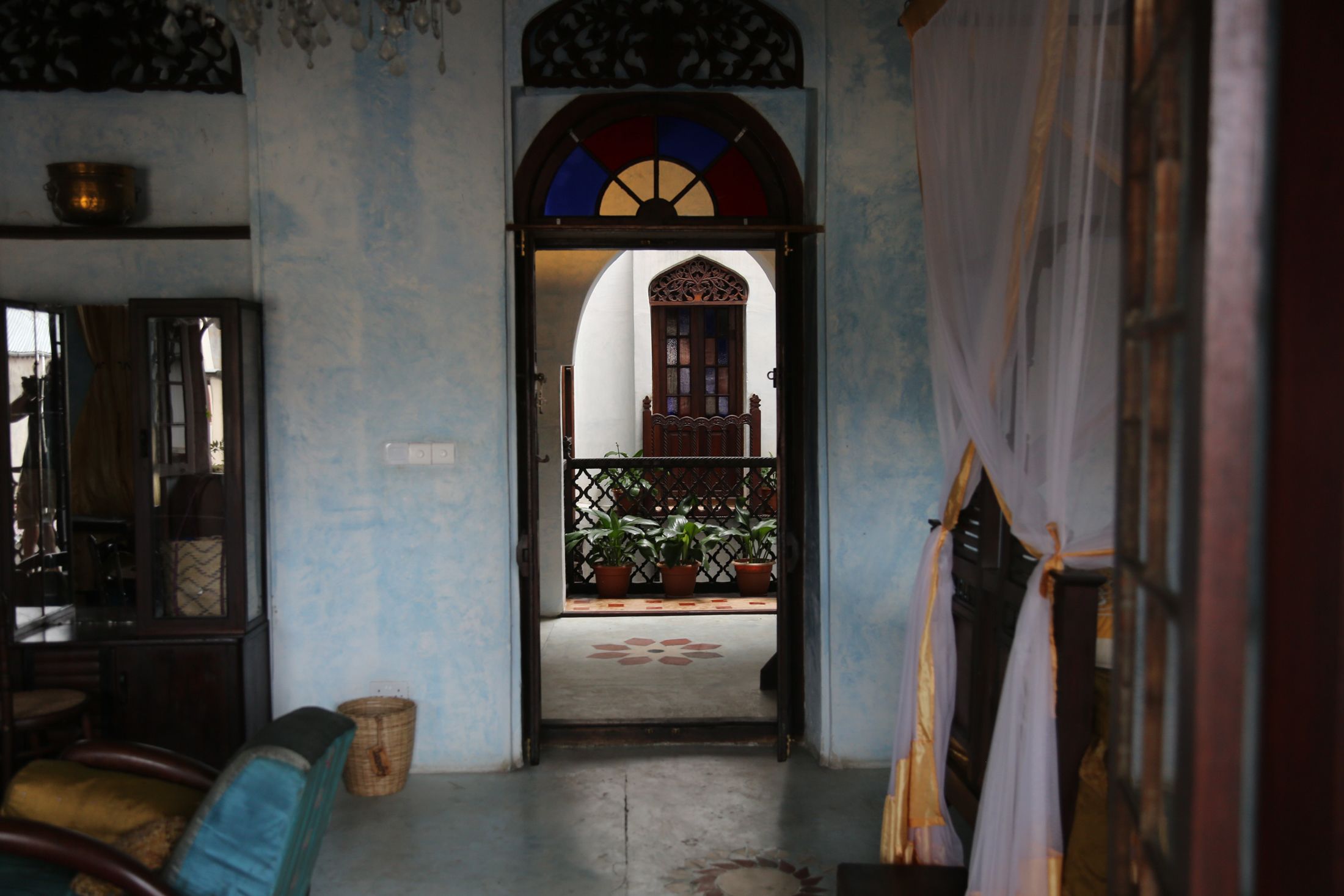 A traditional room with a wooden door, a small balcony with potted plants, and a patterned floor mat.