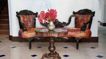 Een traditionele bank met gedetailleerde houten decoraties, een ronde houten tafel met een bloevas, en een vloer met een patroon.