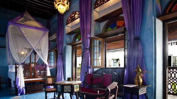 A room with a bed, a chair, a table, and a window with curtains. - Emerson Spice Hotel (Zanzibar Town)