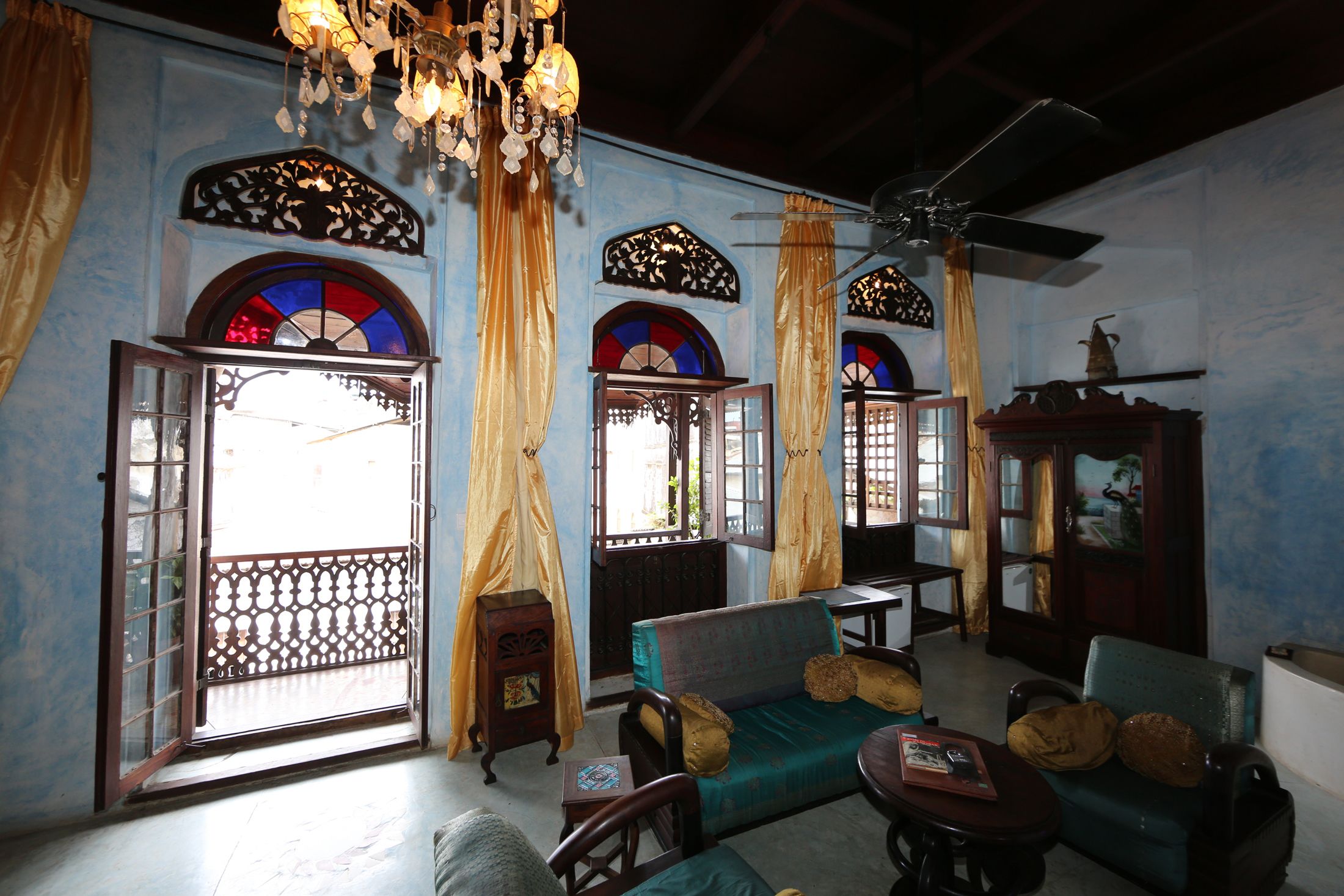 A room with a sofa, a small table, and a cabinet. There are windows with curtains and a chandelier.