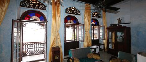 A room with a sofa, a small table, and a cabinet. There are windows with curtains and a chandelier.