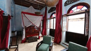 A room with a bed, two chairs, a hanging light fixture, and a window with red curtains.