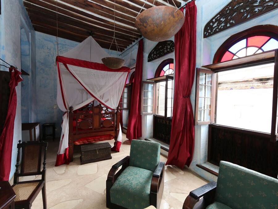 A room with a bed, two chairs, a hanging light fixture, and a window with red curtains.