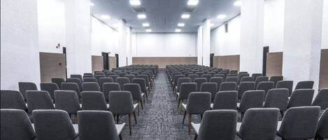 A conference room with rows of grey chairs, a carpeted floor, and white walls.
