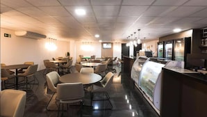 Un restaurante moderno con mesas y sillas redondas, una barra con vitrina y luces en el techo.