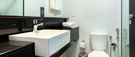 Un baño moderno con lavamanos blanco, encimera negra y cabina de ducha con mampara de vidrio.