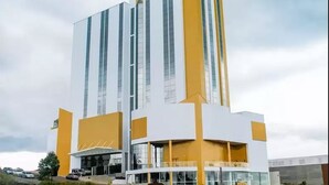 Un hotel moderno con una fachada alta, blanca y amarilla, ventanas amplias y una entrada destacada.