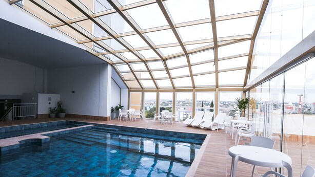 Una piscina interior moderna con techos de vidrio transparente y vistas a la ciudad.