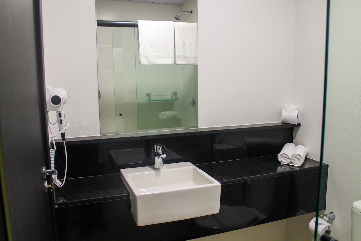 Een badkamer met een zwart aanrecht, een witte wastafel, een glazen douchecabine en een handdoekrek.