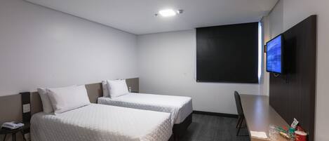 A hotel room with two beds, a desk, a TV, and a small table with snacks.