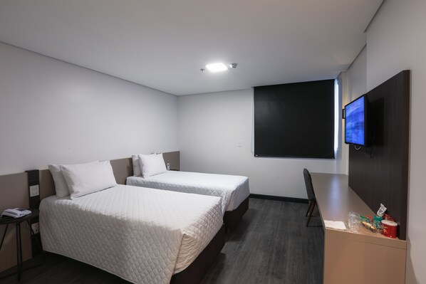 A hotel room with two beds, a desk, a TV, and a small table with snacks.
