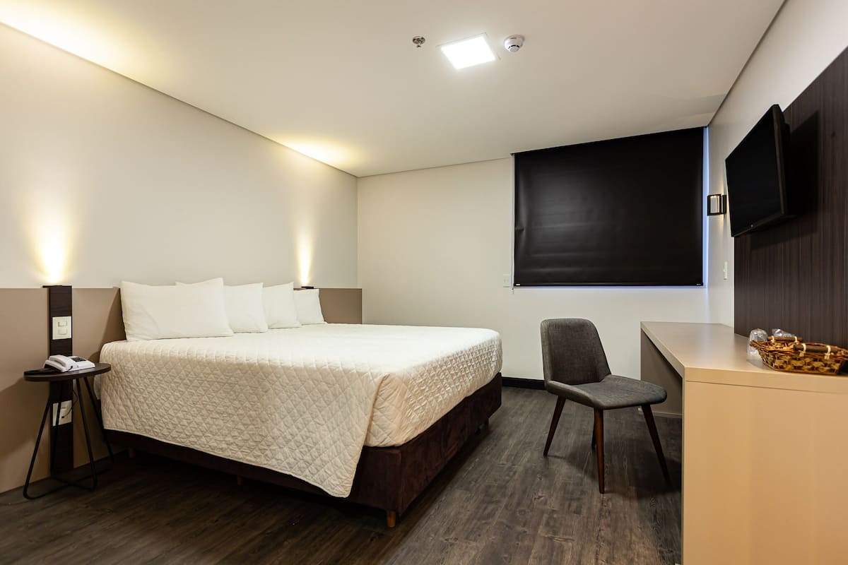 Een hotelkamer met een bed, een bureau, een stoel, een flatscreen televisie en een wandtelevisie.