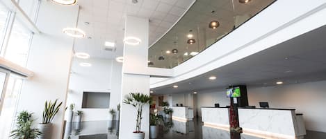 Eine moderne Hotelhalle mit einer Rezeption, Zimmerpflanzen und einer Glastrennwand, die auf die Lobby blickt.