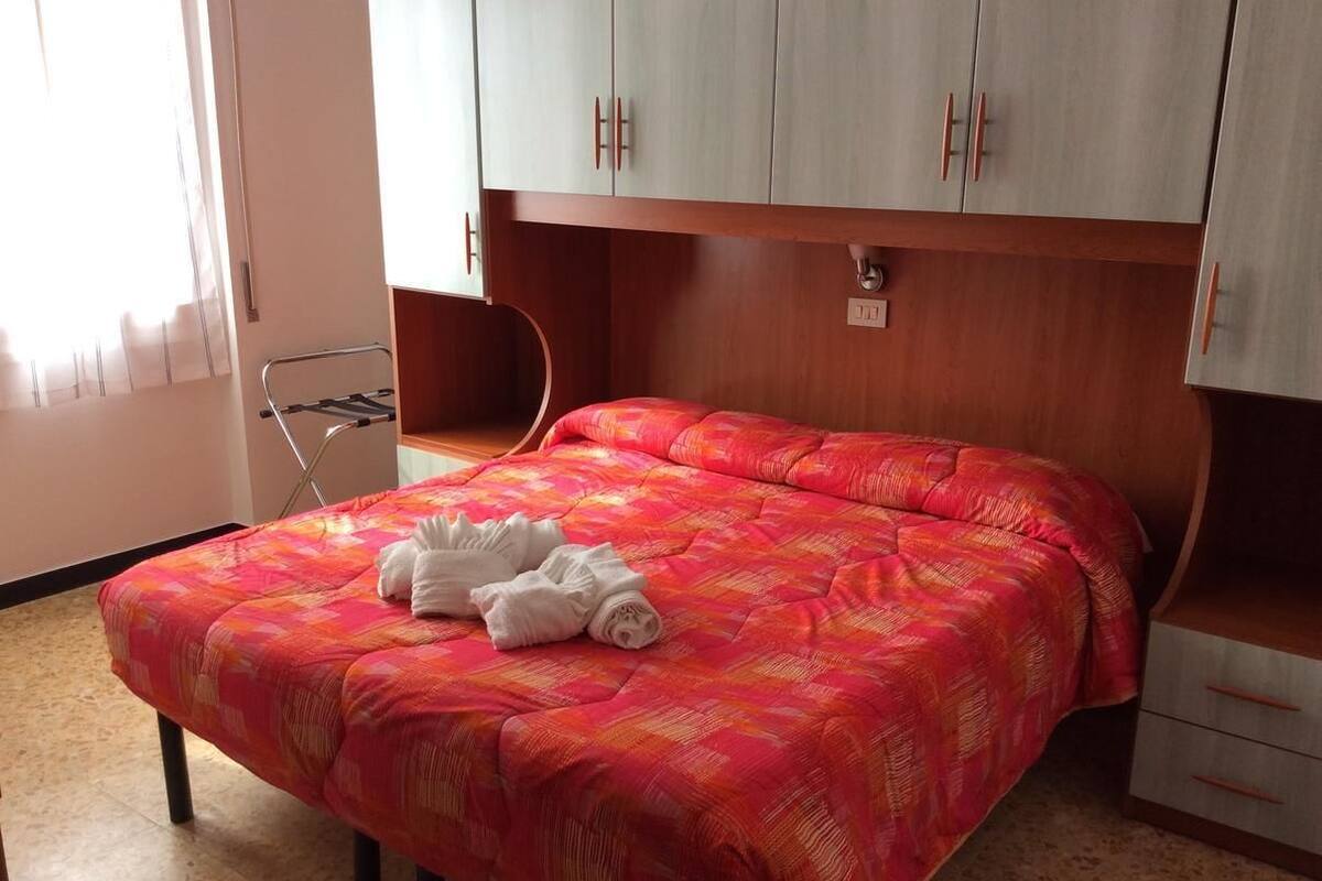 A hotel room with a bed, a wooden headboard, a small desk, and a window with curtains.