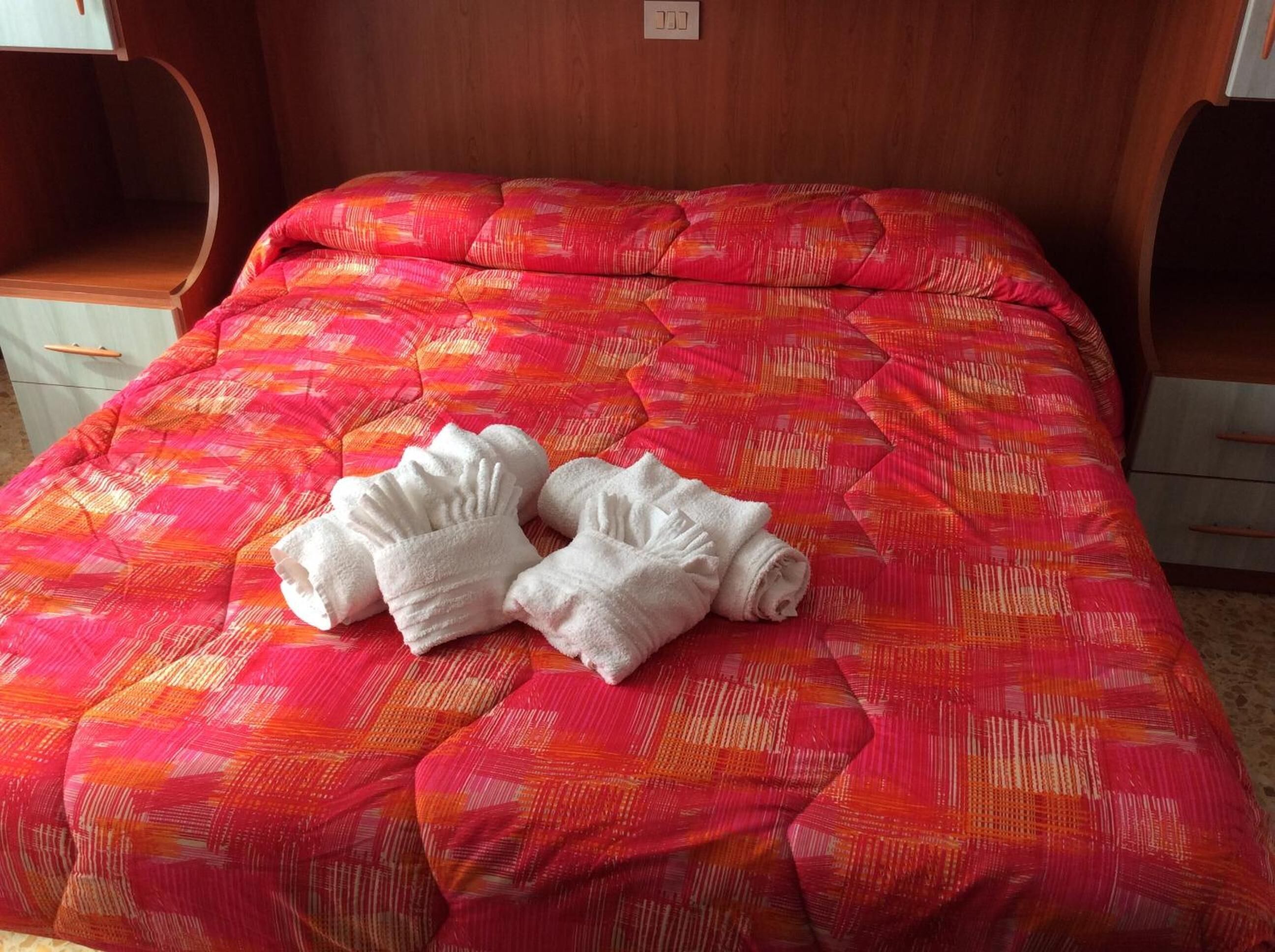 A bed with a vibrant red and orange patterned bedspread and two neatly folded white towels.
