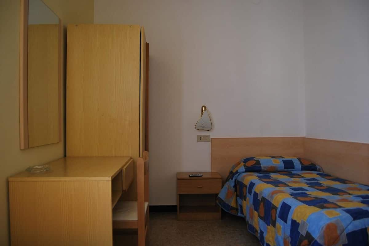 A bedroom with a wooden desk, a bed with a patterned bedspread, and a bedside table with a lamp.