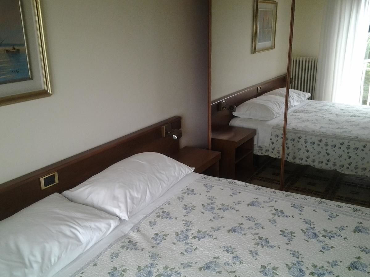 A hotel room with two beds, a wooden headboard, a bedside table, and a mirror.